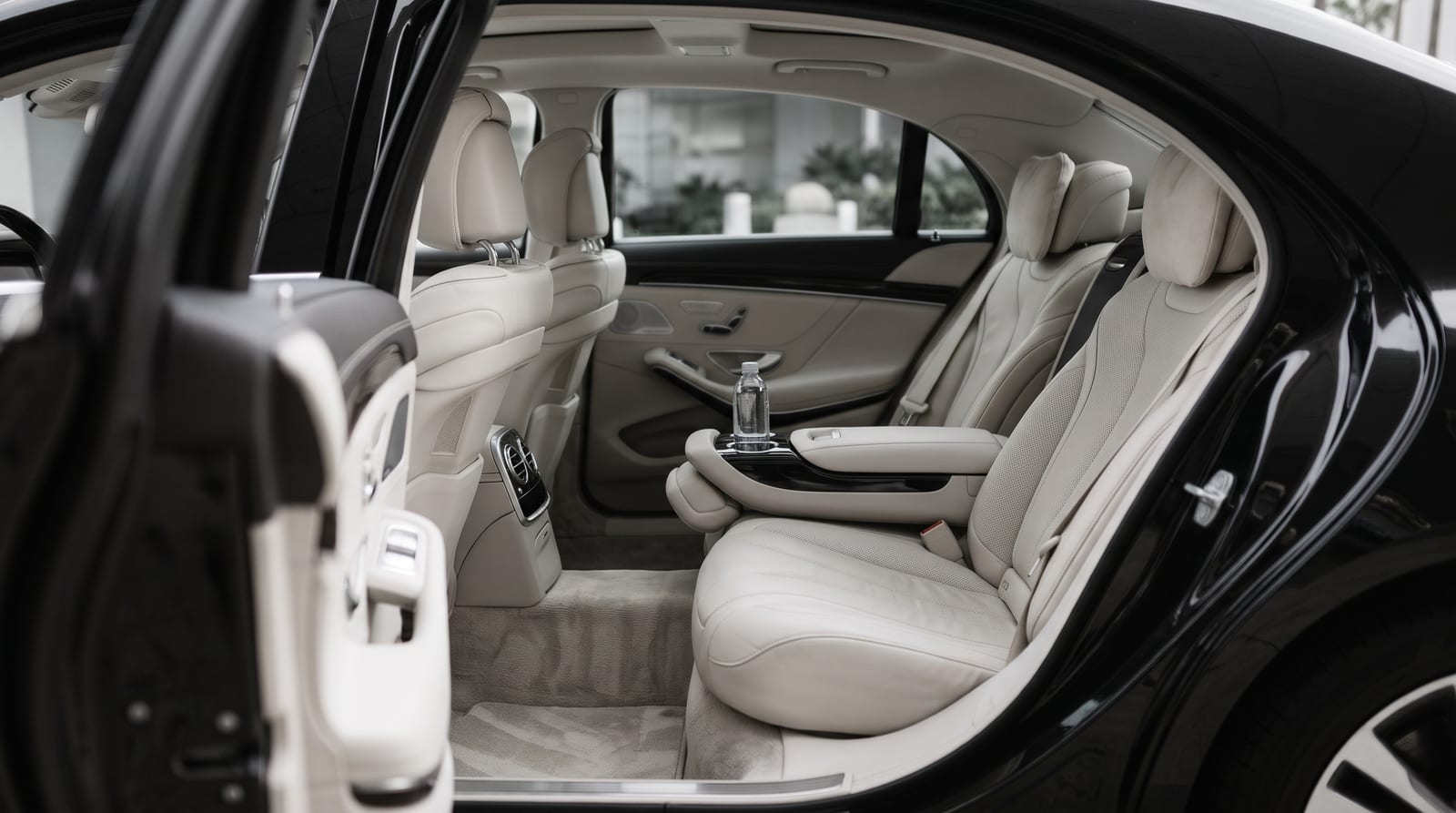 The rear cabin of a black sedan, door open, water in the armrest